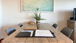 Une table de conférence en bois, avec une œuvre d’art encadrée au-dessus, une plante en pot et un carnet posés sur la table.