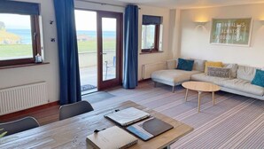 Une pièce avec un canapé, une table sur laquelle sont posés des livres, une vue sur la mer et une citation encadrée accrochée au mur.