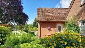 A brick house with a tiled roof, surrounded by lush greenery and flowering plants.