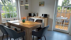 A modern kitchen with a wooden table, black chairs, and a view of the backyard through large windows.