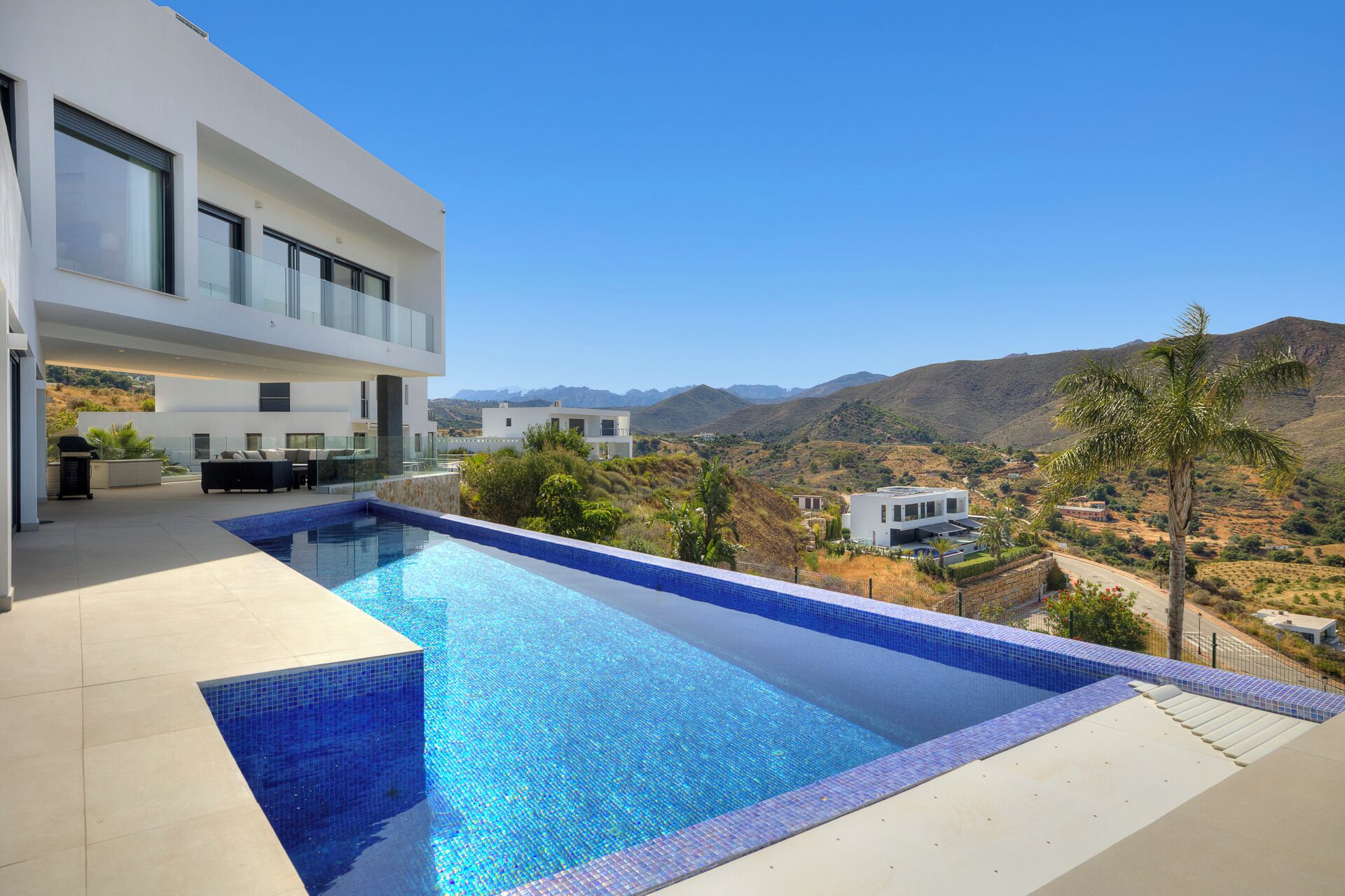 A modern house with a large swimming pool, a patio area, and a view of the surrounding hills.