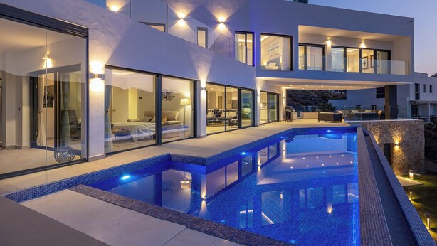 Een modern herenhuis met zwembad, grote glasramen en buitenverlichting.