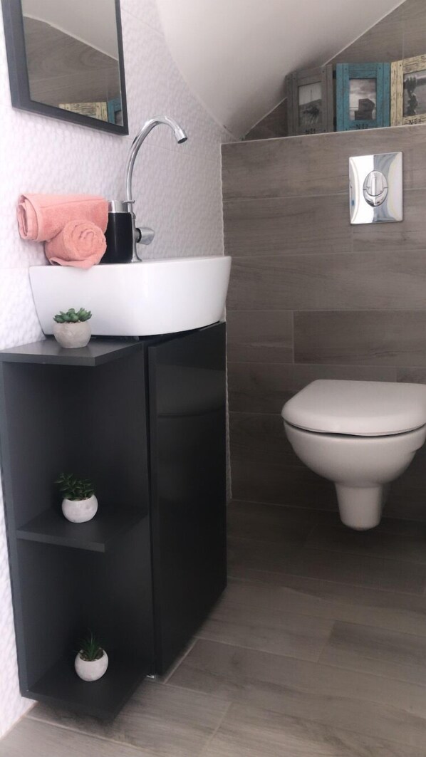 A modern bathroom with a white sink, black cabinet, and a white toilet. There are small potted plants on the cabinet shelves. - Salt&sea Summerhouse Mandre, 30m vom Strand, Garten,whirlpool,meerblick (Mandre)