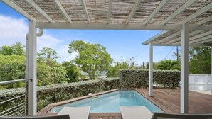 An outdoor pool area with a pergola, lounge chairs, and a view of the surrounding greenery.