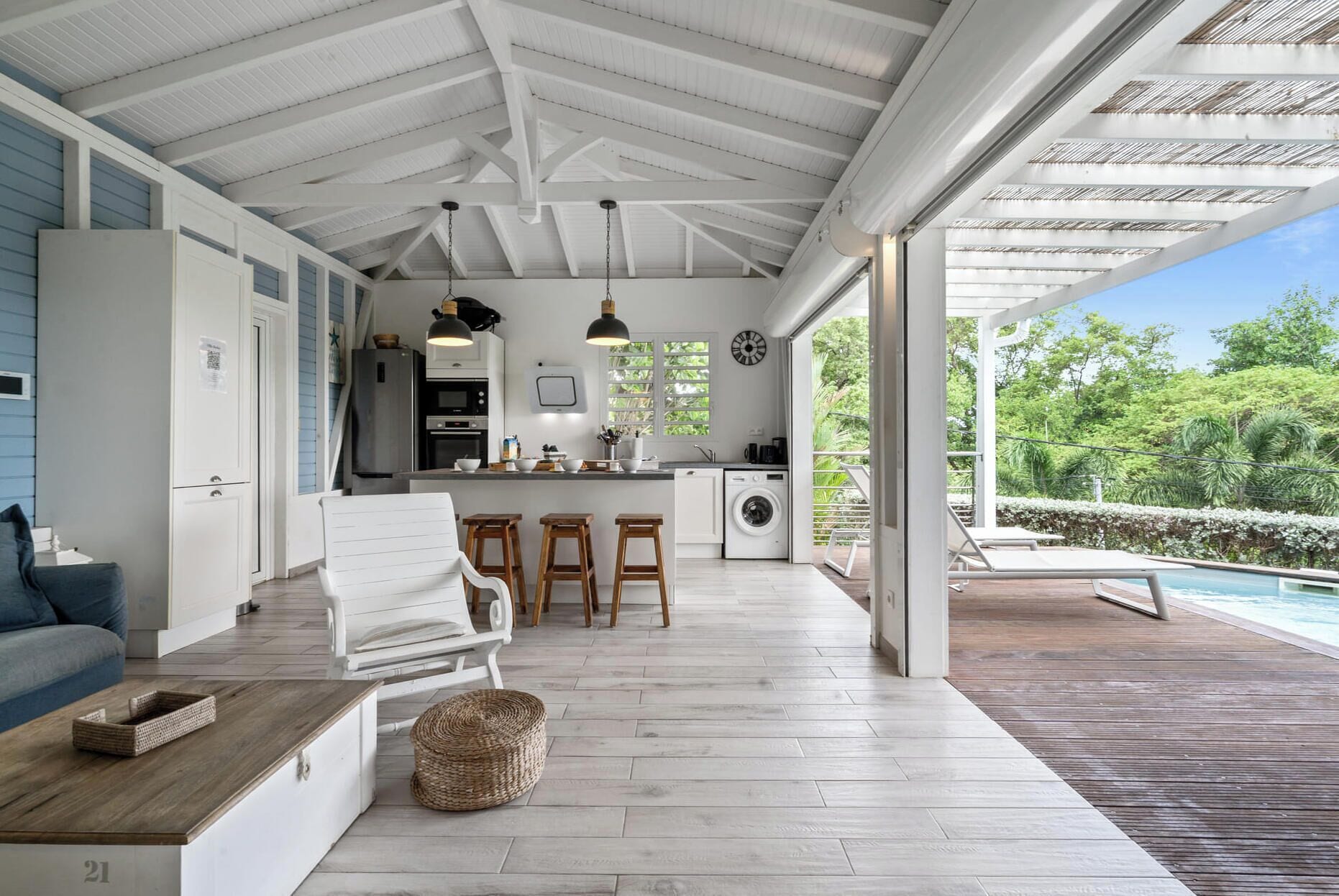 A spacious kitchen with a large island, a dining area with a white chair and stools, and a view of a swimming pool.