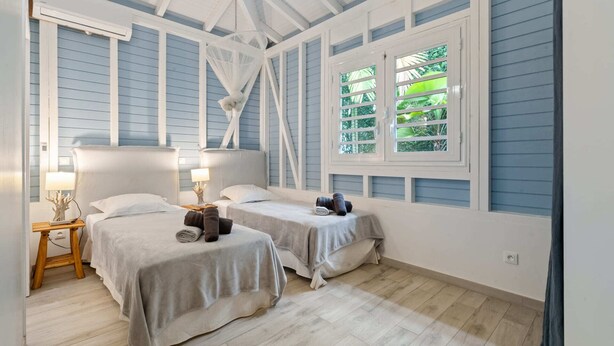 A room with two beds, a hanging chair, and a window with a view of greenery.