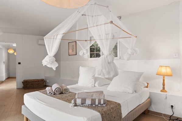 A bedroom with a canopy bed, a bedside lamp, and a wicker basket.