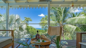 A covered outdoor seating area with a view of the ocean, surrounded by palm trees and a wooden deck.