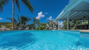 A clear blue pool with lounge chairs and palm trees.