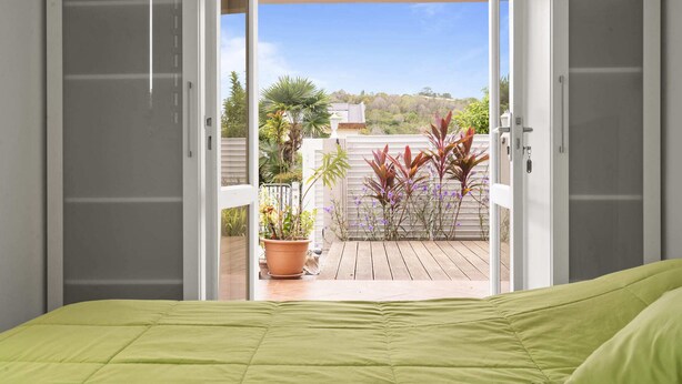 A bedroom with a green bedspread, a view of a balcony with potted plants and a wooden deck. - Villa Kavich - Two Bedroom Villa, Sleeps 4 (Les Trois-Îlets)