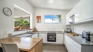 A modern kitchen with white cabinetry, a built-in oven, a sink, and a window with a view of greenery.