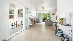 A modern kitchen with a refrigerator, a dining area with chairs and a table, and a living area with a sofa and a lamp.