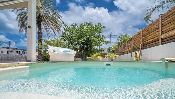 A swimming pool with clear water, surrounded by a wooden fence and palm trees.
