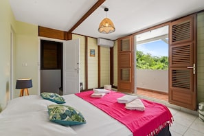 Un dormitorio con cama, almohadas, una lámpara de noche, un equipo de aire acondicionado y vistas a un espacio exterior por una puerta corredera.