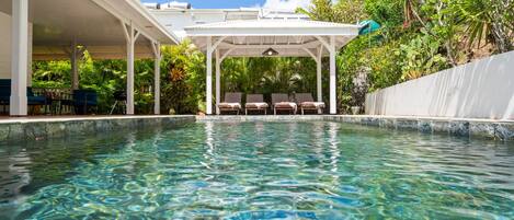 Una piscina cristalina con sillones de descanso y una zona de estar techada.