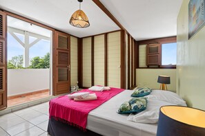 Un dormitorio con cama, lámpara de noche, ventana con persianas y vistas al exterior.