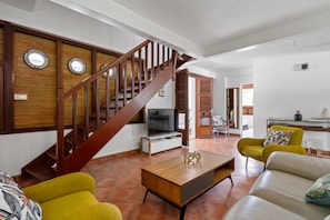 A spacious living area with a wooden staircase, a flat-screen TV, and a coffee table.