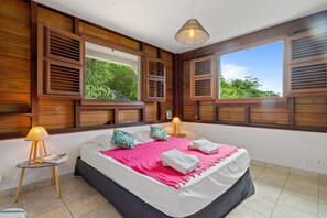 A bedroom with a bed, two bedside lamps, a window with shutters, and a view of greenery outside. - Le petit Dizac - Three Bedroom Villa, Sleeps 6 (Le Diamant)