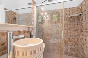 Une salle de bain dotée d’une douche à parois de verre, d’un lavabo en bois et d’un mur carrelé orné de motifs décoratifs.
