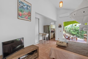 A living room with a TV, a dining area, and a view of a garden.