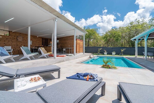 Un área junto a la piscina con sillones reclinables, una zona de estar cubierta y una piscina.