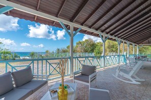 An outdoor patio with seating, a view of the ocean, and a covered area with a tiled floor.