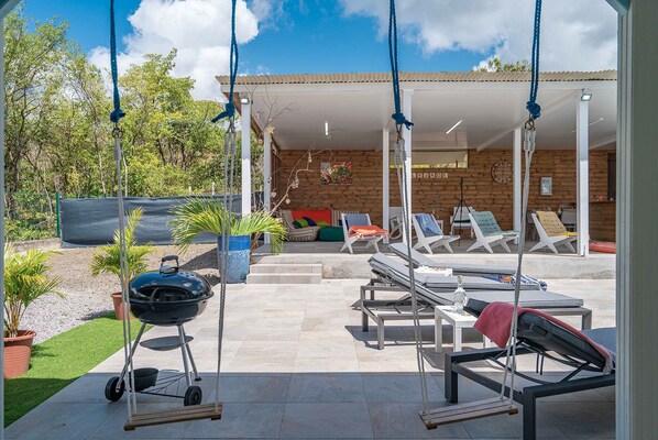 A patio with a swing, a barbecue grill, and lounge chairs.