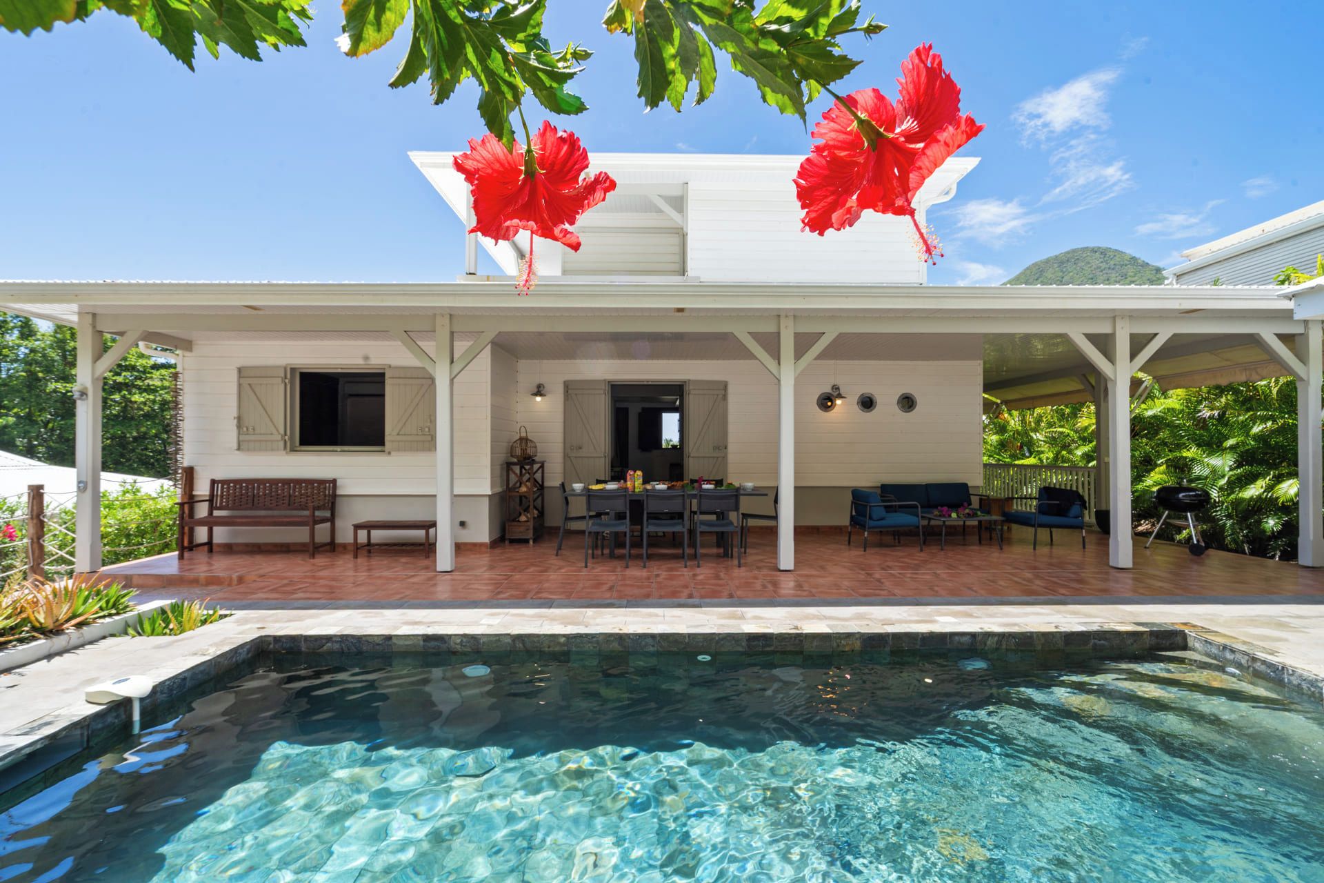 A covered outdoor area with a pool, seating, and a dining table.