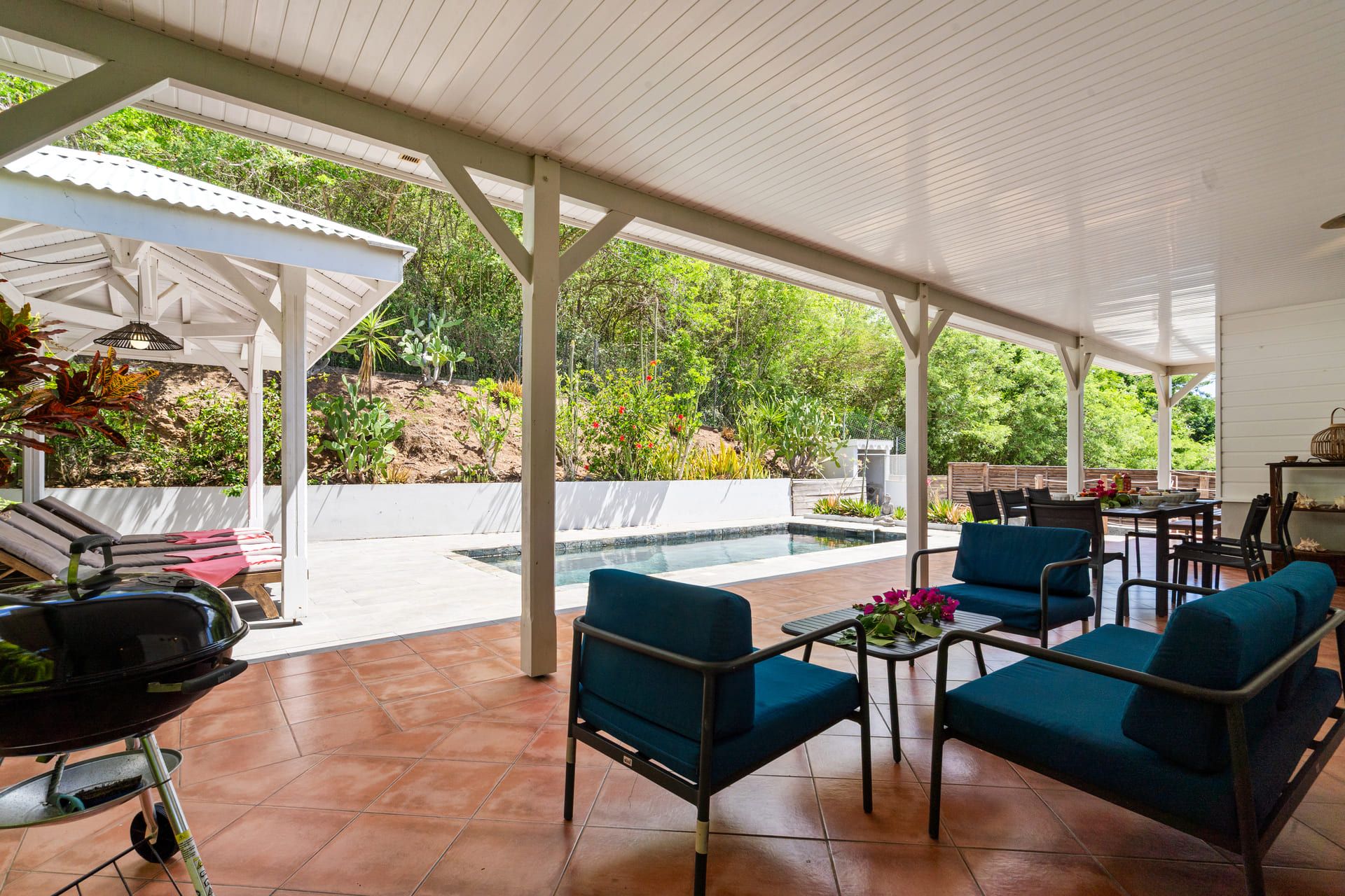 An outdoor patio with a pool, seating area, and a grill.