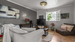 A living room with a grey wall, a flat-screen TV, a sofa, a coffee table, and a window with an open shutter.