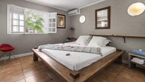A bedroom with a large bed, a red chair, a bedside table, and a window with a view of greenery.