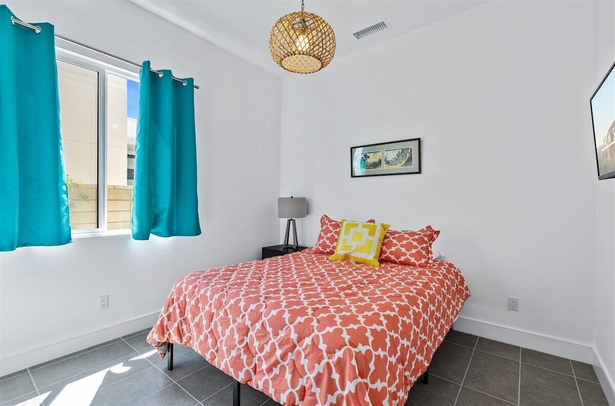 A bedroom with a bed, teal curtains, a wall-mounted picture, and a hanging light fixture.