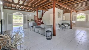 Ein großzügiger Wohnbereich mit Holzbalkendecke, einem grauen Sofa und einem Essbereich mit Stühlen.