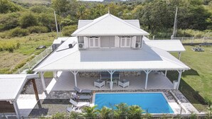 Ein zweistöckiges Haus mit großem Pool, überdachter Terrasse und umzäunter Gartenfläche.