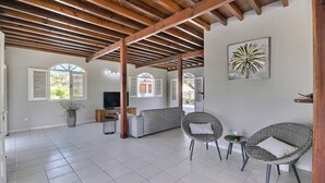 Ein geräumiger Wohnbereich mit Holzboden, einem grauen Sofa, Korbstühlen und einem Fernseher.
