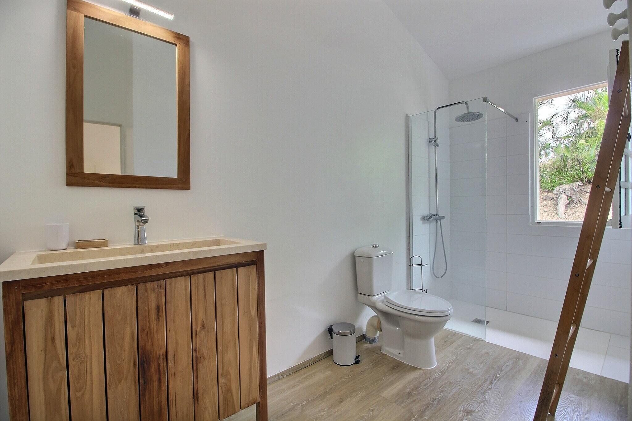 A bathroom with a wooden vanity, a toilet, a shower enclosure, and a large mirror.