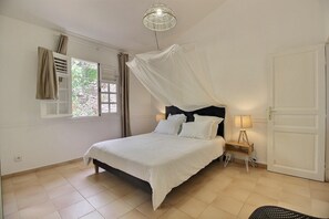 Ein Schlafzimmer mit einem Bett, einer Nachttischlampe, einem Fenster mit Vorhängen und einer Tür.
