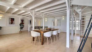 Un comedor amplio con mesa de madera y sillas blancas, una escalera y vistas al exterior.