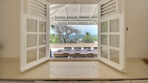 Ventana abierta con vistas a una mesa de comedor preparada para cuatro personas, techo blanco y un árbol afuera.
