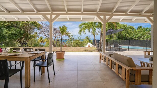 Un patio cubierto con una mesa y sillas de comedor, una planta en maceta y un área de piscina con sillones de descanso.