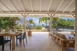 A covered patio with a dining table and chairs, a potted plant, and a pool area with lounge chairs. - Villa Flamboyant - Five Bedroom Villa, Sleeps 11 (Le François)
