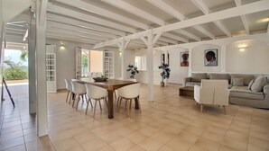 Amplia sala de estar con techo alto y vigas a la vista, una mesa de comedor con sillas, un sofá y vistas al exterior.