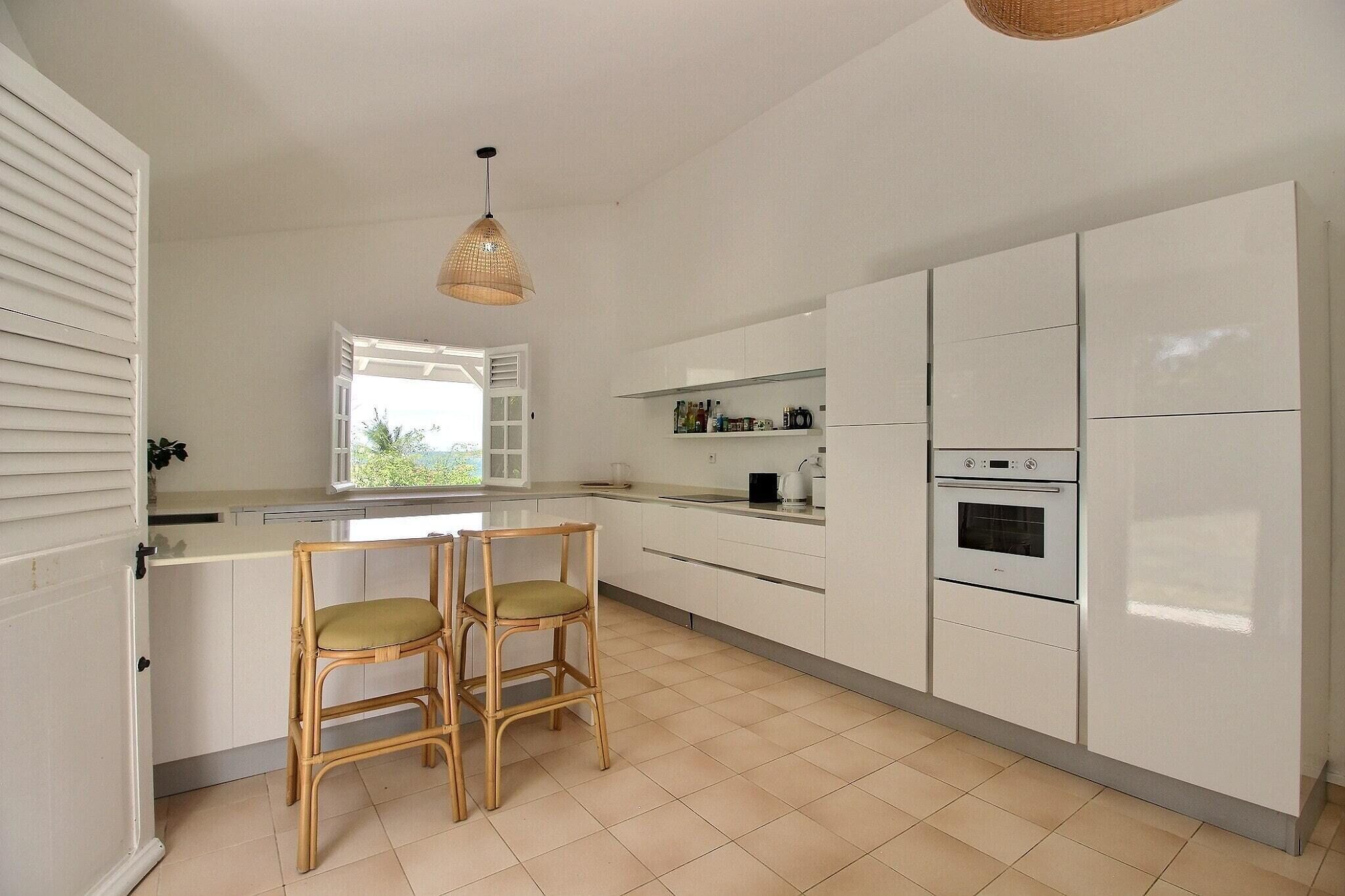 Una cocina moderna con armarios blancos, horno empotrado y zona de comedor con dos sillas.