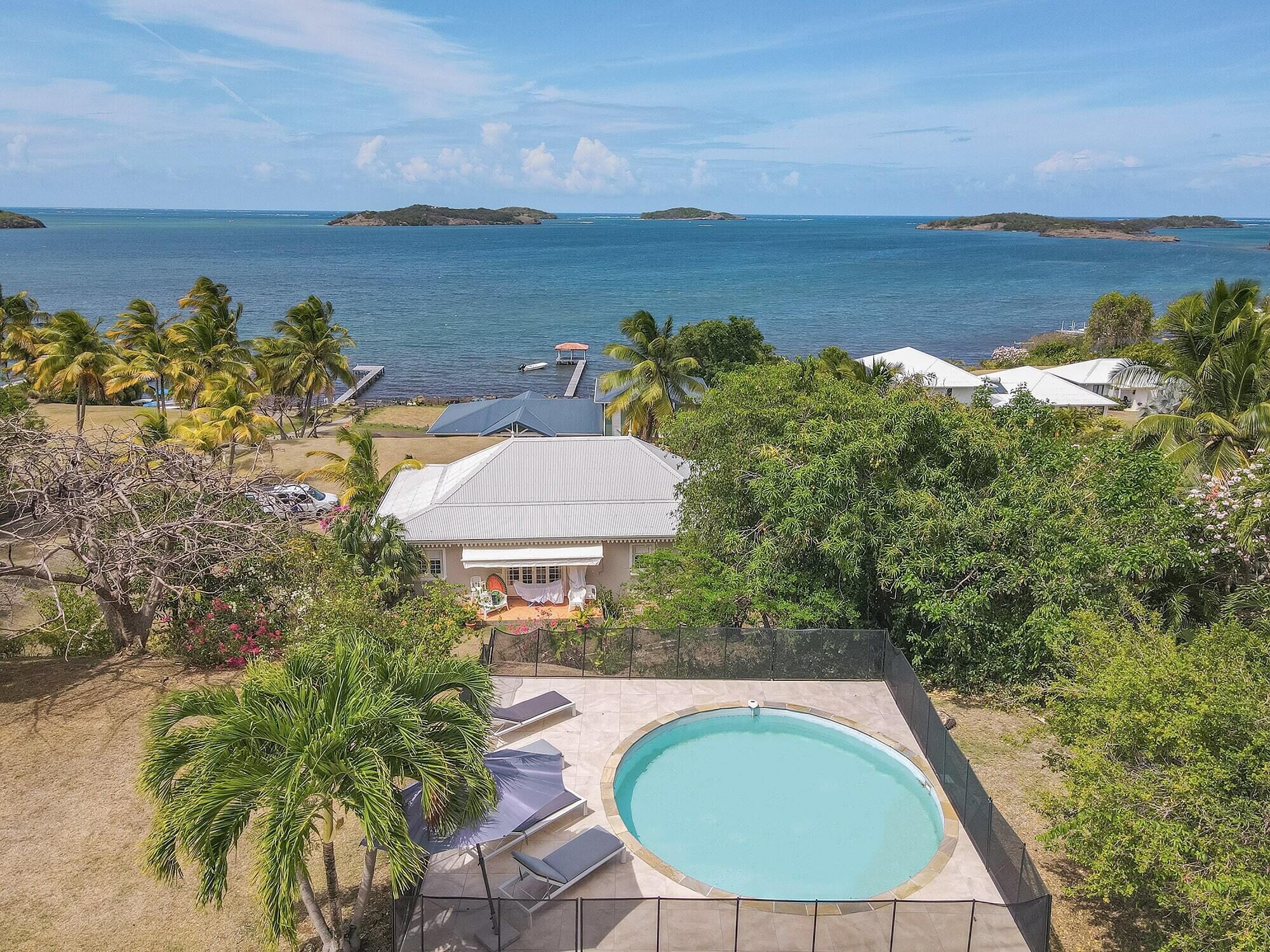 A pool area with lounge chairs, a house with a white roof, and a view of the ocean.