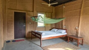 Une chambre avec un lit simple, une moustiquaire, un banc en bois et une porte ornée d’un motif décoratif.
