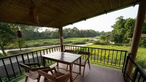 Une table et des chaises en bois sur un balcon donnant sur une rivière et une végétation luxuriante.