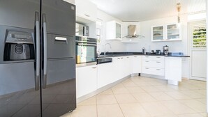 A modern kitchen with a built-in refrigerator, oven, and microwave. It features white cabinetry, a black countertop, and a tiled floor. - Villa Olga - Two Bedroom Villa, Sleeps 4 (Le Vauclin)