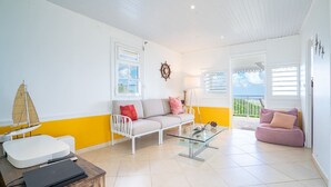 A bright living room with a white and yellow color scheme, a white sofa, a glass coffee table, and a white armchair. - Villa Olga - Two Bedroom Villa, Sleeps 4 (Le Vauclin)