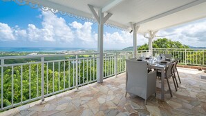 A covered outdoor dining area with a stone floor, white railing, and a table set for two. - Villa Olga - Two Bedroom Villa, Sleeps 4 (Le Vauclin)