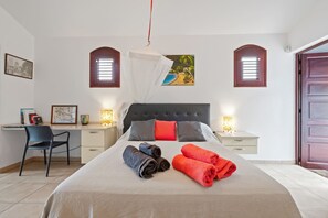 Een slaapkamer met een bed, twee nachtkastjes, een bureau, een stoel en een deur.